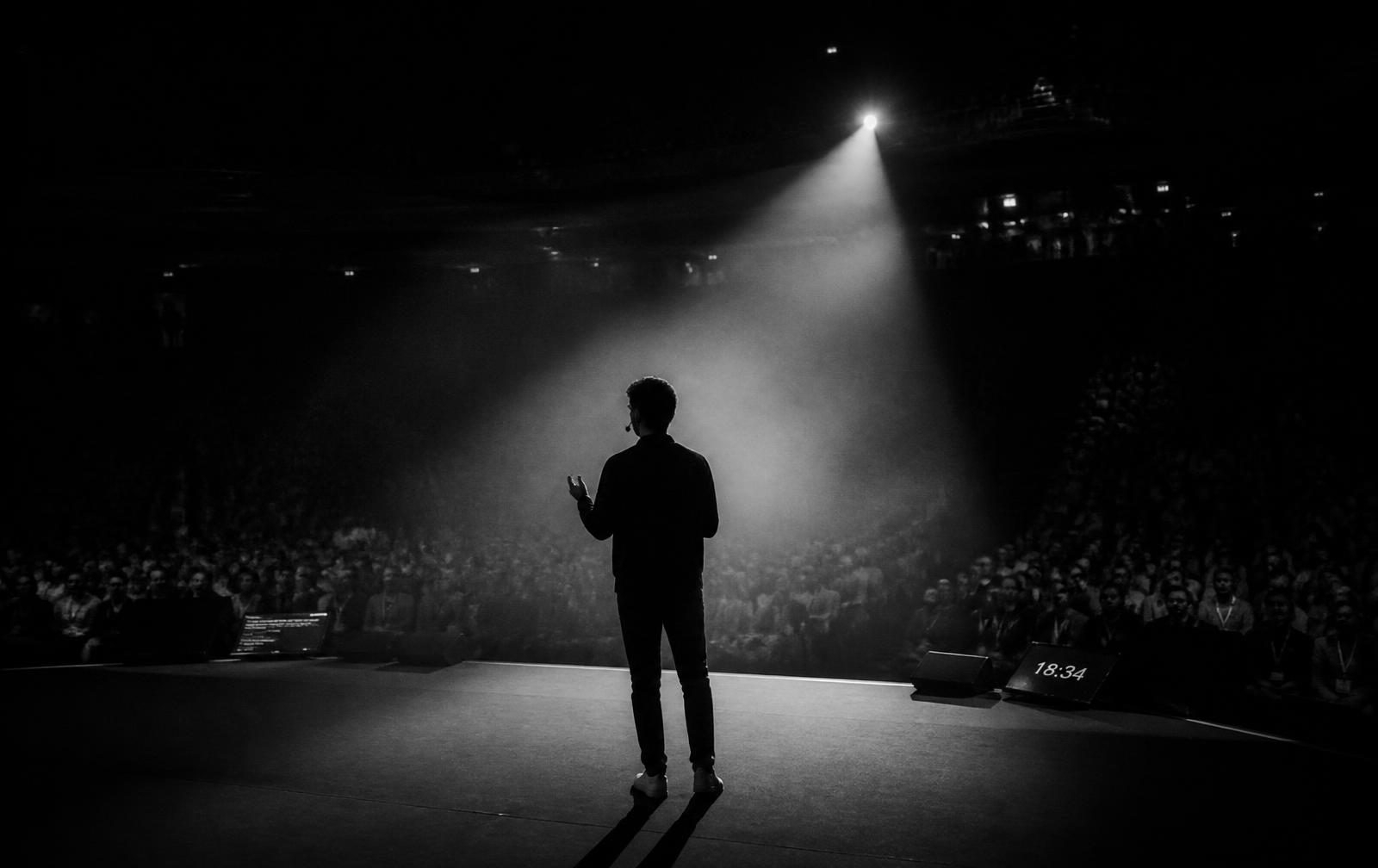 Sir-John Perkins speaking on a large stage under a single spotlight
